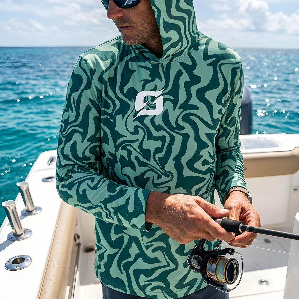 Angler on a center console boat rigging a spinning rod over turquoise water, wearing a hood-up Origin Gear Co. green swirl-camo UPF 50+ performance shirt with the white logo mark on the chest.